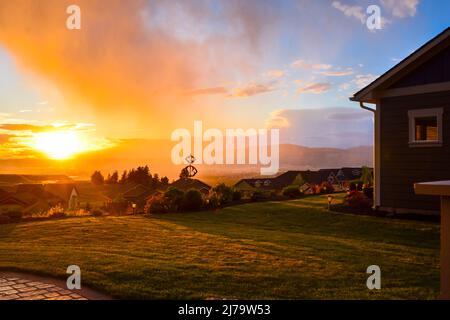 View from a hillside of a suburban neighborhood as a summer rain shower is illuminated in the orange glow of the setting sun Stock Photo