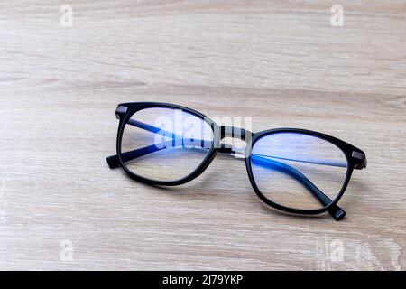 Pair of classic black reading glasses on wooden table. Glasses with filter coating blocking screen's blue light to prevent computer vision syndrome. Stock Photo