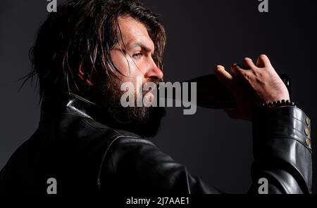 Brutal bearded man in leather jacket drinking beer of bottle. Handsome guy drink alcoholic beverage. Stock Photo