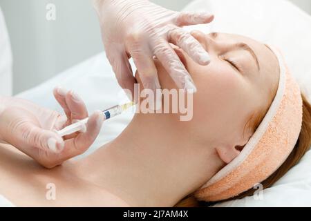 Cosmetologist performs the chin lift procedure by injecting beauty injections. Doctor injecting hyaluronic acid into the ching of a woman as a facial Stock Photo