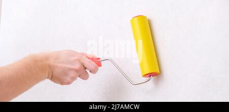 A man rolls out a canvas of white wallpaper with a suture yellow roller. Removing air bubbles and glue. Wallpapering. Repair of a room, apartment, house. Stock Photo