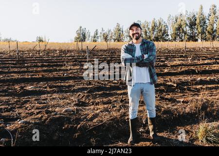 Wide shot of a latin farmer man with crossed arms in the middle of the farmland.  Stock Photo