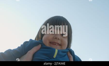 Cute dressed up smiling smiling child or baby is being lifted into the air by his father and they are enjoying this beautiful summer day together by p Stock Photo