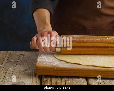 Macro shot. The chef rolls out the dough with a rolling pin on a wooden background. The concept is recipes for dough products - pastries, pasta, pizza Stock Photo