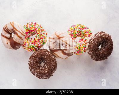 Multi-colored sweet donuts covered with sugar icing, confectionery sprinkles and chocolate in a frozen flight on a white background. Sweet food, calor Stock Photo