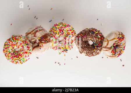 Sweet donuts decorated with icing sugar, chocolate and confectionery sprinkles in a frozen flight on a white background. There are no people in the ph Stock Photo