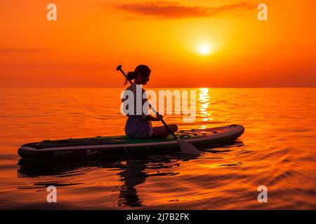 June 21, 2021. Antalya, Turkey. Woman on stand up paddle board at quiet sea with sunset or sunrise. Woman on Red Paddle sup board and bright sunset in Stock Photo