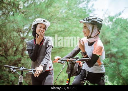 two young muslim women chatting while cycling together Stock Photo