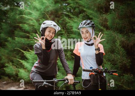 two women in veil with ok hand gesture while cycling Stock Photo