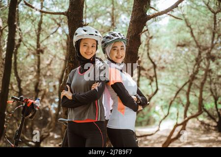 two smiling veiled women standing back to back while cycling Stock Photo