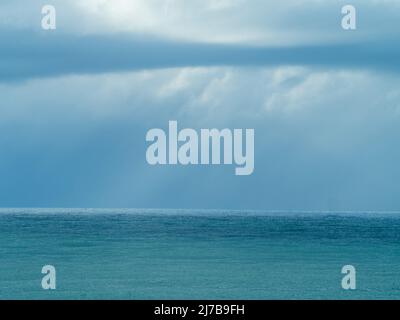 All the blues in sea and storm, layers of blue green and grey, sun shining through clouds Stock Photo