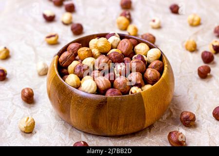 Peeled brown hazelnuts in round wooden bowl on light background. Stock Photo