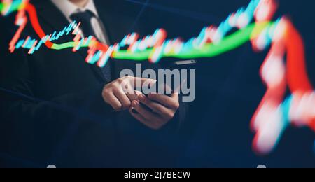 Man using smartphone with graphs analysis candle line and foreign currency rate on bokeh colors light. Manager analyzing investment statistics and ind Stock Photo