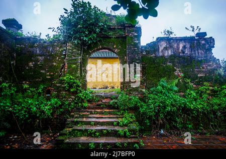 Old wall at Hue VN., with an archway entrance and no door with brick walls overgrown with moss and fungi. Mysterious entrance. Stock Photo