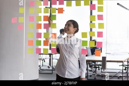 Happy millennial Indian business woman working at Kanban board Stock Photo