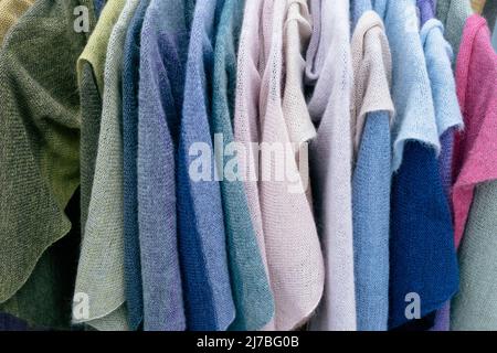 Women's multicolored knitted and crocheted sweaters, jackets hang on hangers in the store. Stock Photo