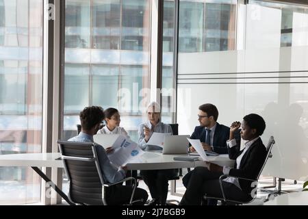 Serious adult female business leader instructing diverse team Stock Photo