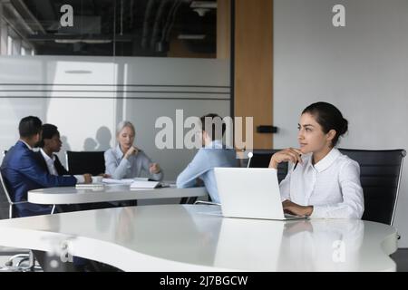 Thoughtful young Indian employee woman using laptop in co-working space Stock Photo