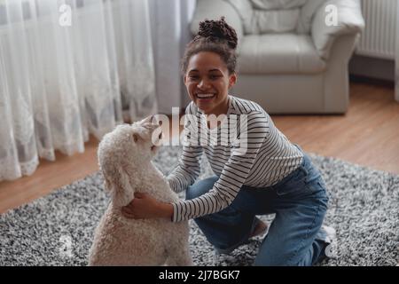 Top view of cheerful smiling young woman palying with poodle dog indoors at home Stock Photo