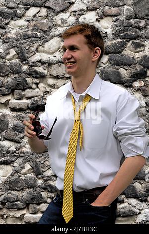 Young man standing next to blended stonewall with sunglasses in his hand. Stock Photo