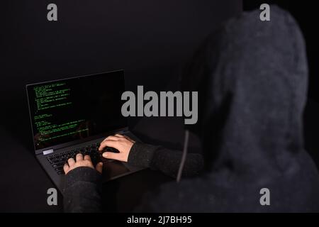 Concept of hacking and malware. Hacker using an abstract laptop with a binary code digital interface. Young hacker in cybersecurity concept. Stock Photo