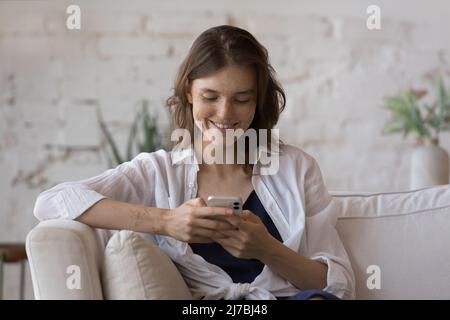 Happy freckled smartphone user girl sitting on couch at home Stock Photo