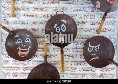 Old frying pans with painted faces, hang on a brick wall, close up Stock Photo