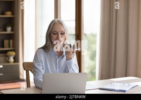 Happy grey haired freelance business lady using virtual assistant Stock Photo