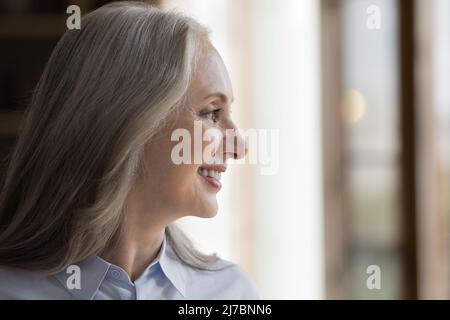 Happy pretty mature woman looking out of window away Stock Photo