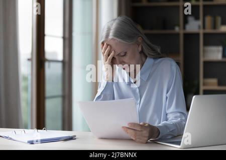 Frustrated worried mature business woman reading paper documents Stock Photo