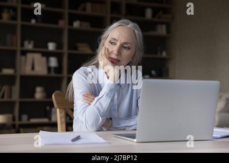 Serious senior business woman working at laptop computer at home Stock Photo