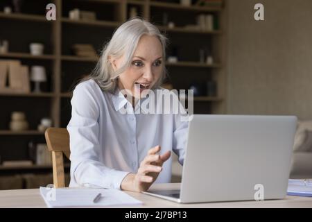 Shocked happy middle aged laptop user woman staring at display Stock Photo