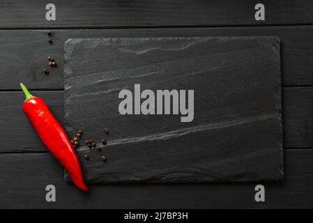 square slate board in dark color. chili peppers and spices on black background layout with space for text, top view Stock Photo
