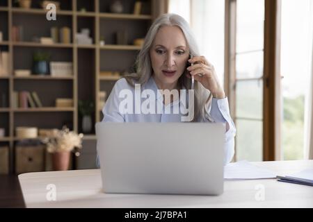 Happy mature 50s business professional woman answering mobile phone call Stock Photo