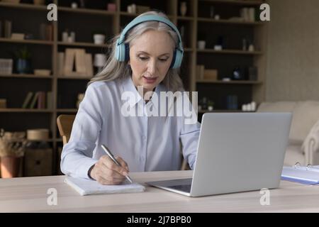 Focused older student in wireless headphones watching virtual workshop Stock Photo