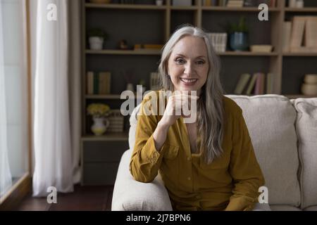 Happy cheerful pretty senior lady sitting on couch at home Stock Photo