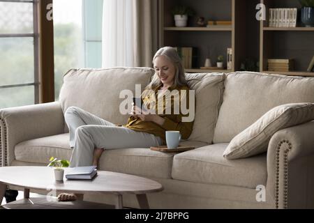 Cheerful grey haired lady using mobile phone at home Stock Photo