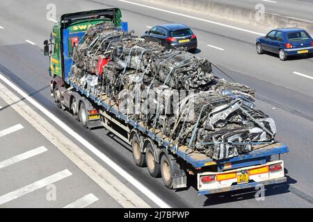 Aerial side back view of crushed scrap metal car bodies loaded on flatbed articulated trailer towed by hgv lorry truck driving along UK motorway road Stock Photo