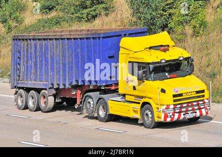 Haulage contractor business yellow bonneted hgv SCANIA lorry truck blue unmarked dirty articulated tipper trailer driving along on English UK motorway Stock Photo