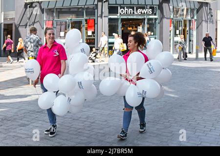Two young women holding clusters of white balloons giving them away free to promote window cleaning business summertime in Chelmsford Essex England UK Stock Photo