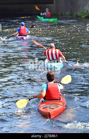 Back view of four guys paddling Kayaks along River Can on a sunshine summer day approaching a road bridge Chelmsford town centre Essex England UK Stock Photo