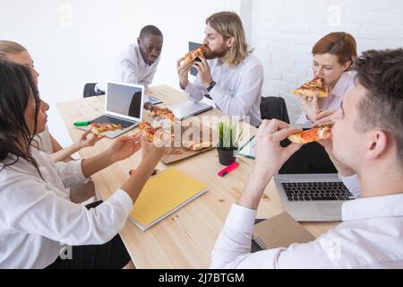 Diverse business team people workers eating pizza together at workplace, friendly multi-ethnic colleagues group talking enjoying having fun and corpor Stock Photo