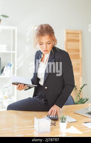 Attractive business woman counting with calculator and making notes in a notebook Stock Photo