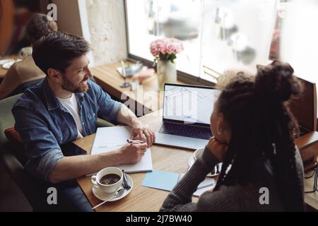 Couple of happy startupers working at laptop in cafe. Business talk at coffee break. Brainstorm. Stock Photo