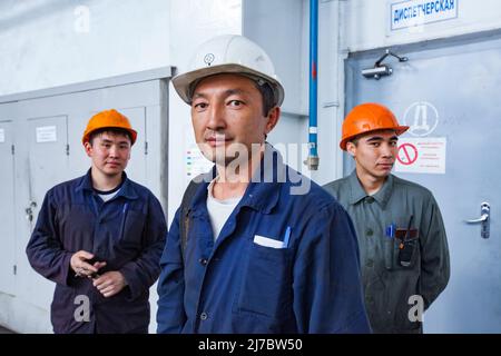 Ust'-Kamenogorsk, Kazakhstan - May 31, 2012: Three Asian men, two workers and engineer (in center, white work helmet) on titanium metallurgy plant. Te Stock Photo