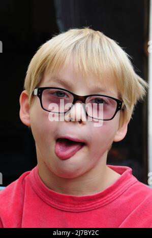 portait of a young boy wearing glasses on his head sticking his tongue out , concept of being silly bully funny face . Stock Photo