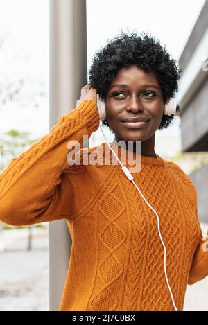 African American woman listening to music with headphones while standing outdoors on the street. Stock Photo