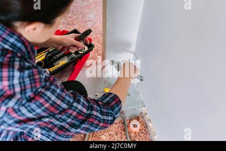 Female plumber tightening pipe with wrench in heating installation Stock Photo