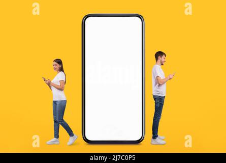 Couple standing near white empty smartphone screen and using phones Stock Photo