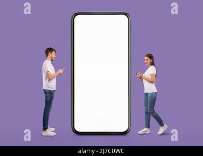 Couple standing near white empty smartphone screen and using phones Stock Photo